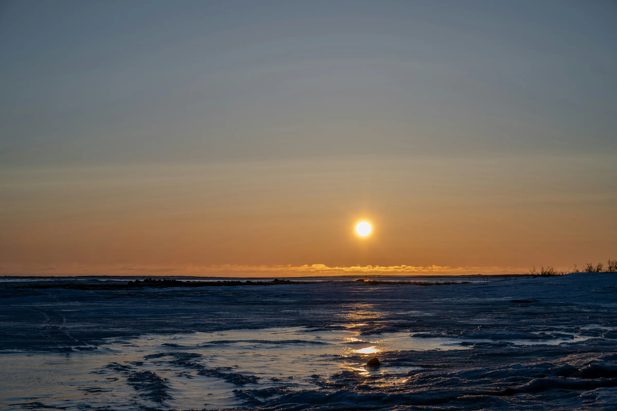 The sun sets over a frozen body of water