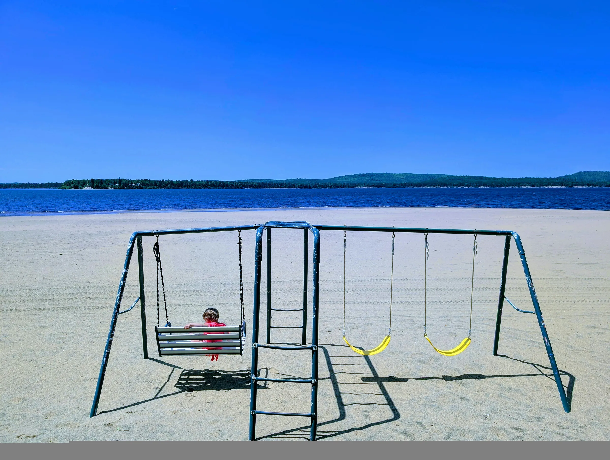 Child sits on a swing set at a sandy beach